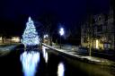 Cotswolds Christmas Scene : The world famous Bourton-On-The-Water Christmas Tree, placed and reflected in the River Windrush, is surrounded by the first sprinkling of Winter snow on the river's banks Monday 29th November 2021 in Gloucestershire. The